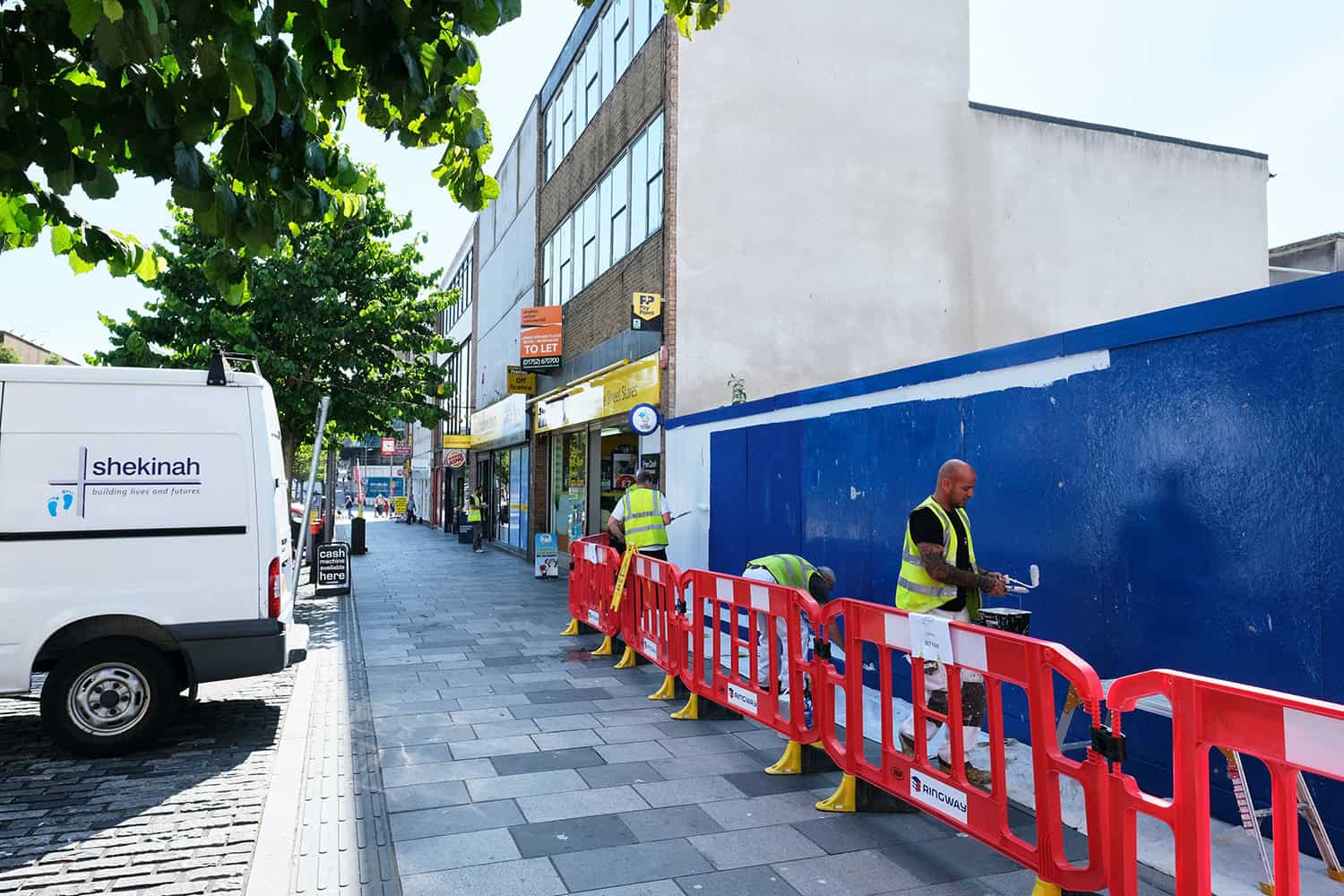 Shekinah Mission Plymouth volunteers in hi-viz painting blue hoarding at West End Plymouth.